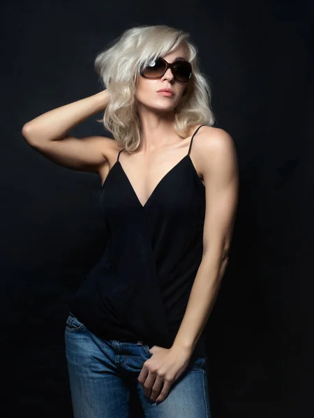 Beautiful blonde woman wearing sunglasses posing over black back — Stock Photo, Image