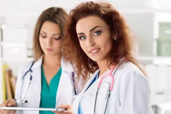 Retrato de duas médicas de pé com prancheta e mesa — Fotografia de Stock