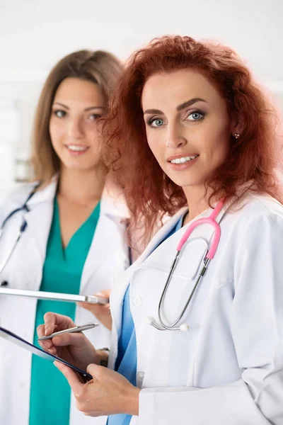 Retrato de duas médicas de pé com prancheta e mesa — Fotografia de Stock