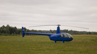 Bulutlu gökyüzüne karşı çimlerin üzerinde mavi özel bir helikopter