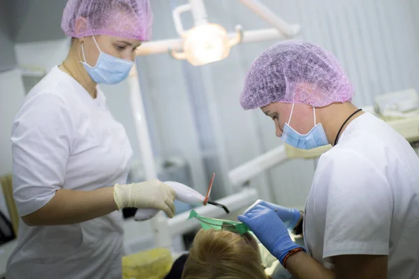 Una dentista y su asistente en uniforme blanco examinan a una paciente. Medicina, Odontología . —  Fotos de Stock