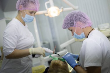 Kadın bir dişçi ve beyaz üniformalı asistanı bir hastayı muayene ediyor. İlaç, Diş Hekimliği.