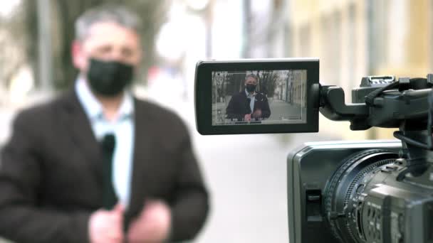 Seorang jurnalis berusia menengah Eropa dalam topeng medis pelindung melaporkan di sebuah kota terpencil. — Stok Video