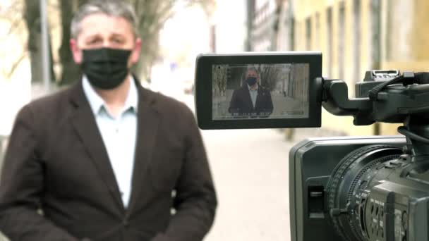 En medelålders europeisk journalist med skyddande medicinsk mask rapporterar i en övergiven stad. — Stockvideo