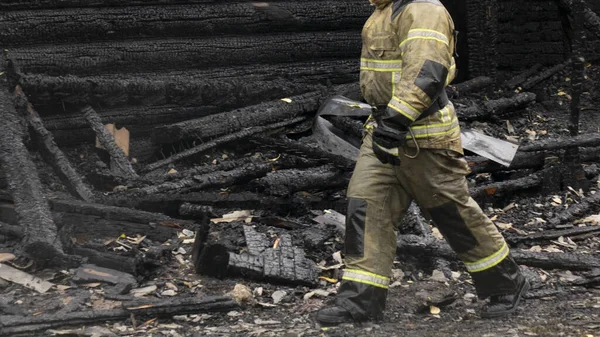 Un bombero en una casa de madera quemada  . — Foto de Stock