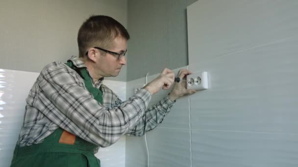 Elektrikern använder en skruvmejsel för att fästa uttaget på väggen. — Stockvideo