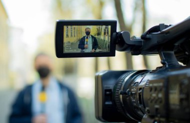 Orta yaşlı, koruyucu tıbbi maskeli Avrupalı bir gazeteci ıssız bir şehirde rapor veriyor..