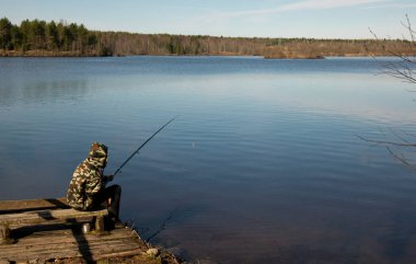 Gölün kıyısında kamuflajlı bir balıkçı. Suda bir oltayla balık tutmak..