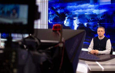 Bir yayın stüdyosunda erkek bir haber spikeri teleprompter 'da metin okur. Kamera TV stüdyosunda..