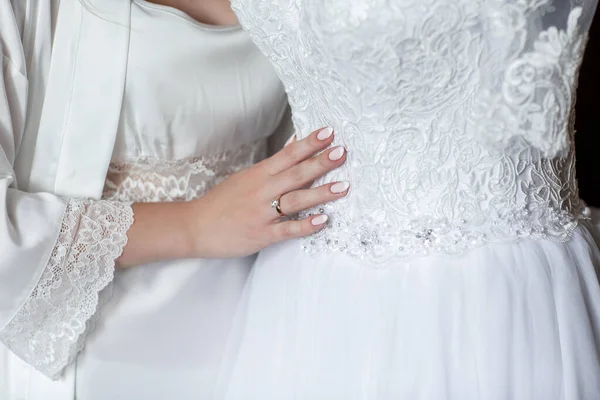 Tolles Kleid. schöne junge Frau im seidenen Bademantel, die ihr Hochzeitskleid berührt. Detail eines eleganten weißen Hochzeitskleides — Stockfoto