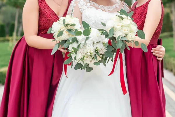 A menyasszony és a koszorúslány virágcsokrot tart a kezében. A koszorúslány a háttérben van. A menyasszonynál esküvői csokor van. Esküvő. Részlet — Stock Fotó