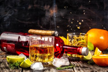 Alkolizm, yalnızlık, bağımlılık kavramı. Bir şişe viski, bir bardak viski ve buzlu, siyah bir masanın üstünde dumanlı bir puro..
