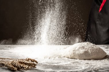 Fırıncı, mutfak masasında nefis pişirmek için hamur hazırladı. Adam taze hamurun üzerine un serpiyor.