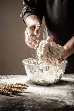 Siyahlı bir aşçı hamuru mutfakta ekmek pişirmek için cam bir kase içinde yoğurur. Ellerinde dışkı