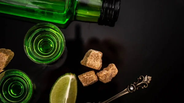 Absinthe ou liqueur à la menthe. absinthe en verre avec des tranches de citron vert sur fond sombre. Alcool, spiritueux de luxe et idée conceptuelle de liqueur dangereuse avec. vue de dessus — Photo