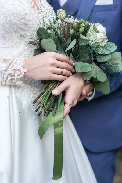 Γαμπρός και νύφη κρατιούνται χέρι-χέρι στο μπουκέτο των λουλουδιών. μπουκέτο στα χέρια της νύφης — Φωτογραφία Αρχείου