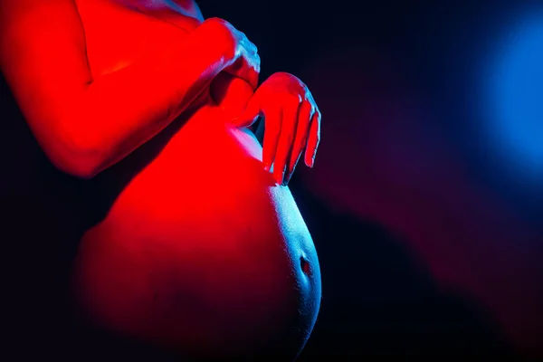 Close-up van de buik van zwangere vrouw op gradiënt studio achtergrond in neon licht. Concept van menselijke emoties. plaats onder de tekst — Stockfoto