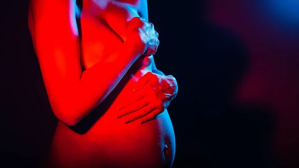 Închiderea femeii însărcinate care se ține de mână pe burtă și așteaptă un copil. Studio în lumină neon. Conceptul emoțiilor umane. Locul sub text — Fotografie, imagine de stoc