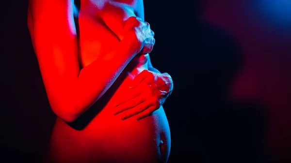 Closeup of pregnant woman holding hand on belly and expecting baby. Studio in neon light. Human emotions concept. place under the text Royalty Free Stock Images