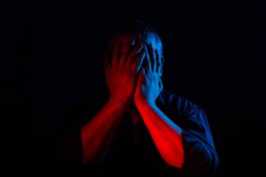 Neon ışıklı bir adamın yakın plan portresi. İnsani duygular, yüz ifadesi, baş ağrısı, yüzdeki eller. İnsan duyguları kavramı