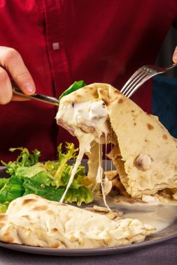 Esneyen peynir. Hamur içinde peynir. Peynirli Focaccia. Peynirli Calzone. Parçayı alan el. restoran ortamı.