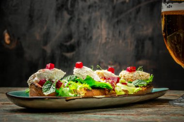 Eski ahşap bir masanın üzerinde taze buğday birası ile servis edilen çiftlik evi ekmeğine farklı çeşitlerde yayılan doyurucu atıştırmalıklar. Somon, peynir, fesleğen. Metnin altına yerleştir.