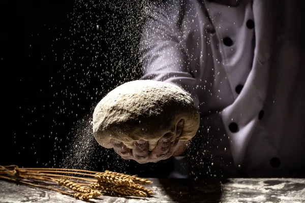 Beautiful and strong men's hands knead the dough from which they will then make bread, pasta or pizza. A cloud of flour flies around like dust. Food concept.