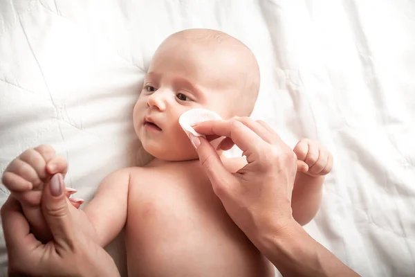 母親の手は白い綿のパッドで新生児の顔を拭く 赤ちゃんの顔を拭く コンセプト衛生洗浄 清潔で清潔なワイプ 赤ちゃんの清潔で柔らかい体の肌のケア — ストック写真