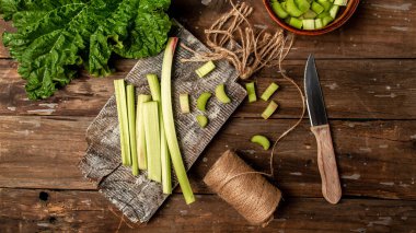 Rubarb sapları. Eski ahşap bir masada taze ravent kökleri ve yaprakları. Ravent pişiriyorum. Pankart biçimi. Metin için boşluk. en üstteki görünüm.