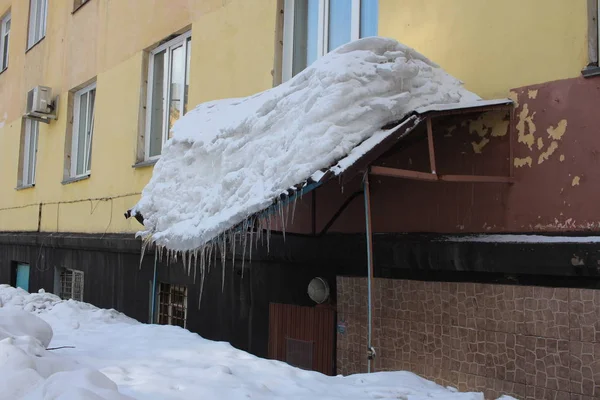 雪の重さの下でバックルされたWindows上の屋根の危険なオーバーハング保護キャノピーは冬に重いつららから破れた — ストック写真