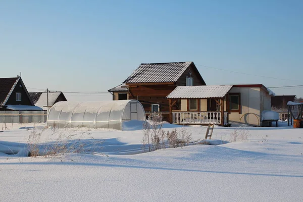 wooden garden house with greenhouse and greenhouse in the snow in winter Siberian village