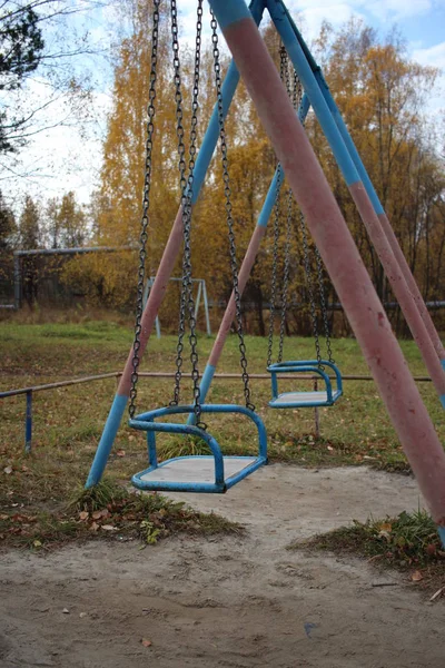 old empty metal children\'s swing on the street in the yard in the fall