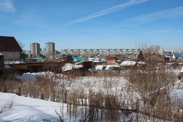 wooden summer cottages in winter in a garden community in the snow near a modern city with a fence in the village