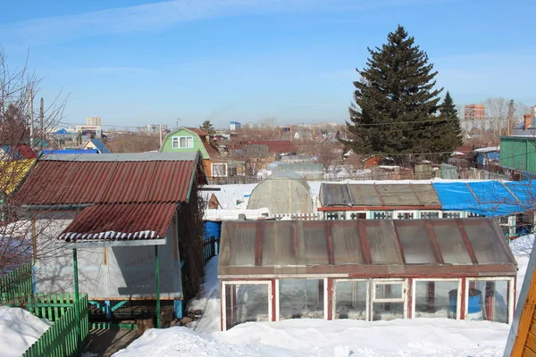 wooden summer cottages in winter in a garden community in the snow near a modern city with a fence in the village