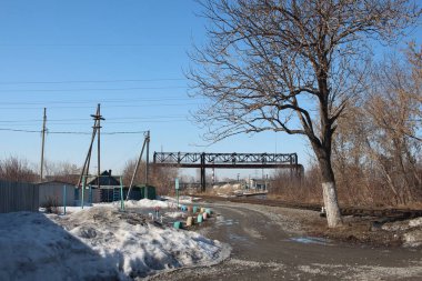 İlkbaharda Sibirya 'da bir köyde, sanayi bölgesinde tren istasyonu olan bir kar yığınının yanında toprak yol.