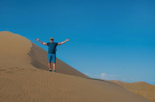 男は砂丘の上で腕を上げている 砂漠の風景と日没 — ストック写真