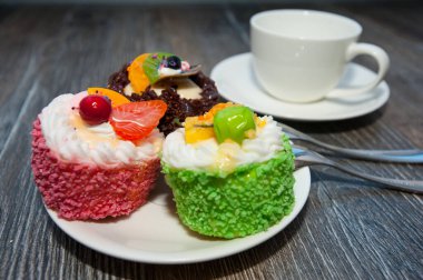 Mini renkli tatlı kekler beyaz tabakta. Çay, kahve ve kaşık için bir fincan. Tatlı. 