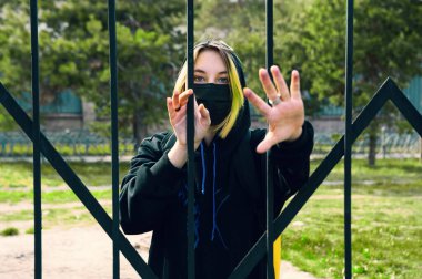 Yüz maskesi takmış bir genç dışarıdaki çitin içinden içeri bakıyor. Kız karantinada kalacak..