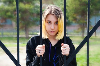 Dişi bir genç kız çitin içinden dışarı bakıyor. Kız karantinada kalacak..