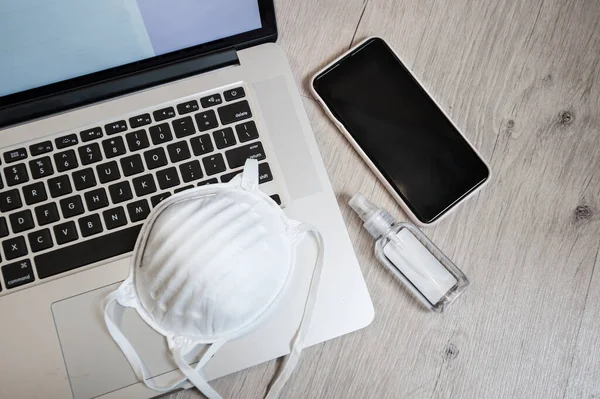 Evden çalışıyorum. Koronavirüsten korunma konsepti. Telefon ve ilaç maskeli dizüstü bilgisayar, dezenfekte jeli. Çevrimiçi çalışıyor
