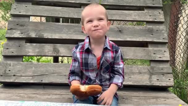 Kleine Schattige Jongen Zittend Een Houten Bank Brood Etend Buiten — Stockvideo