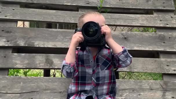 小さなかわいい男の子が大きなカメラで遊んでいる 子供は写真カメラを探索する — ストック動画