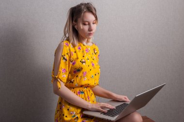 Sarı elbiseli genç kız evde oturuyor ve laptopuyla çalışıyor. Evde kal.