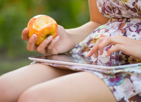 young woman eat apple and play on tablet pc in park