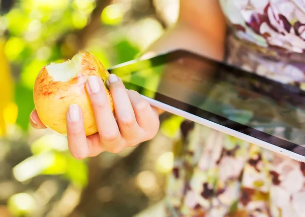 Mujer joven comer manzana y jugar en la tableta PC en el parque — Foto de Stock