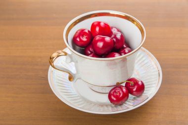 İki cherrie ile ahşap bir masa üzerinde beyaz bir fincan tatlı kiraz