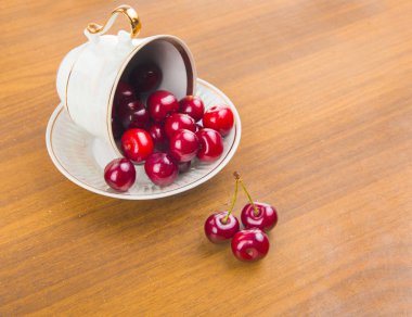 İki cherrie ile ahşap bir masa üzerinde beyaz bir fincan tatlı kiraz
