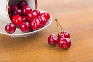 İki cherrie ile ahşap bir masa üzerinde beyaz bir fincan tatlı kiraz