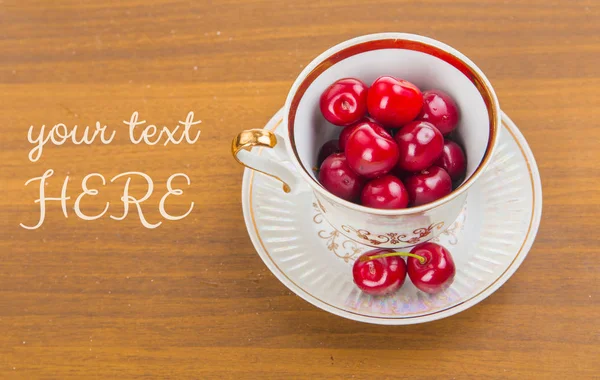 Cerezas dulces en una taza blanca sobre una mesa de madera con dos cerezas —  Fotos de Stock