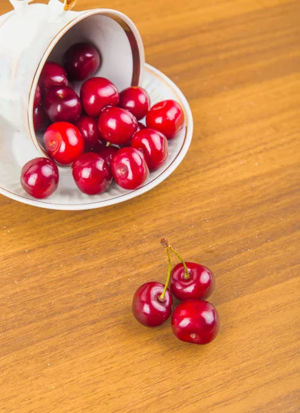Cerezas dulces en una taza blanca sobre una mesa de madera con dos cerezas —  Fotos de Stock